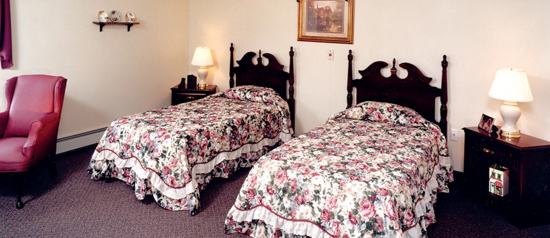 A cozy bedroom with two twin beds featuring floral bedding, a bedside lamp, and a painting on the wall.