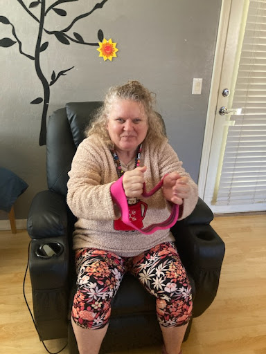 A woman sitting comfortably in a chair, showcasing her colorful outfit and warm smile.