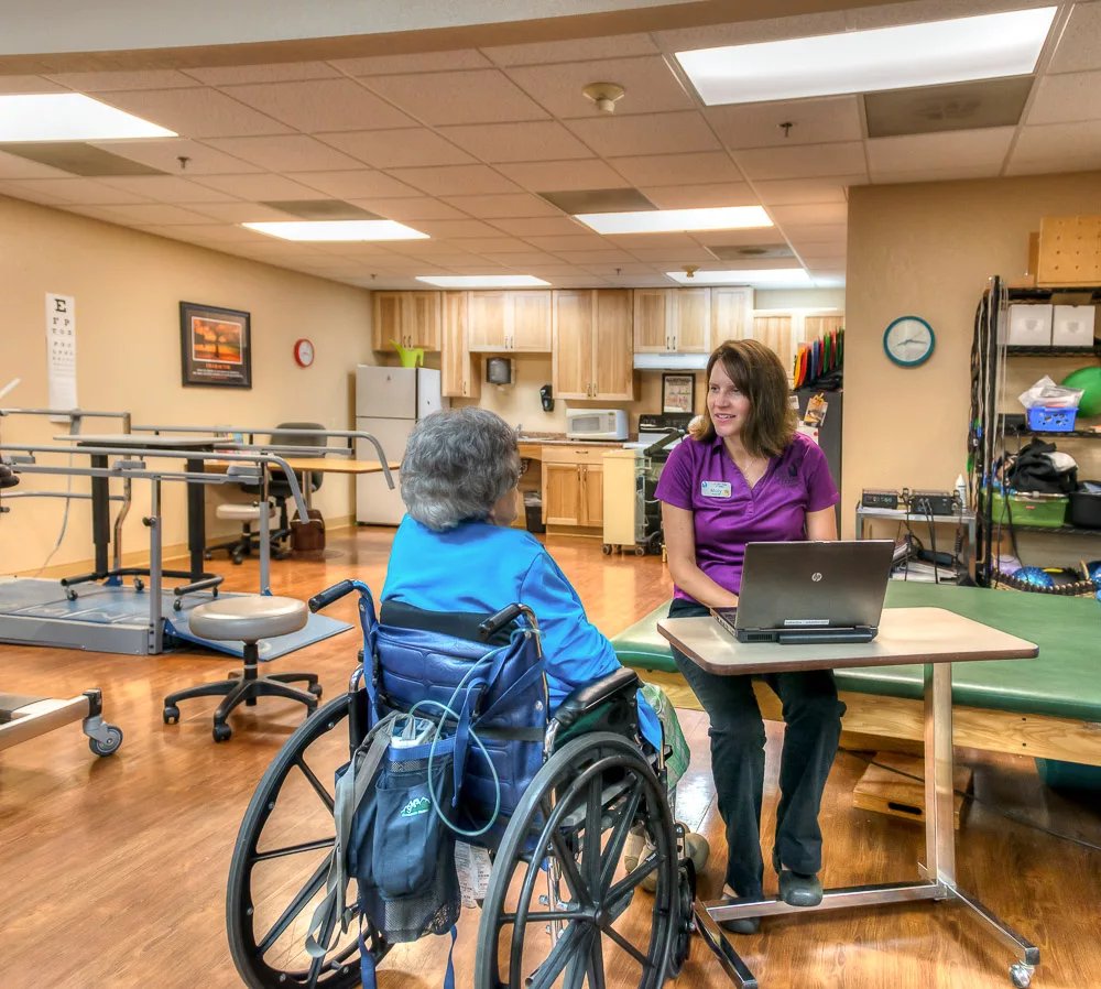 A therapist engages with a patient in a wheelchair during a rehabilitation session in a healthcare facility.
