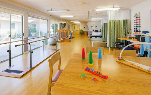 A spacious and well-lit activity room in a rehabilitation center, featuring colorful toys and therapy equipment.
