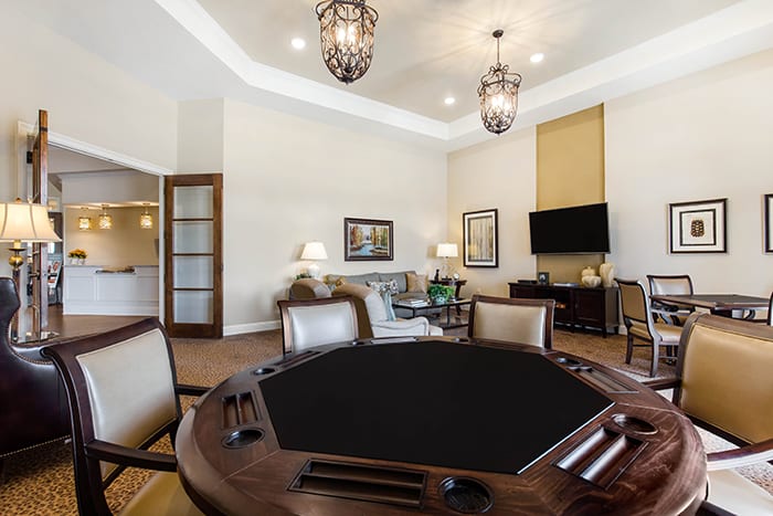 A spacious game room featuring a poker table, elegant chandeliers, and a cozy seating area with a television.