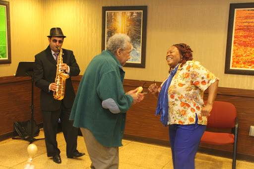 A lively dance scene featuring two seniors enjoying music while a saxophonist plays in the background.