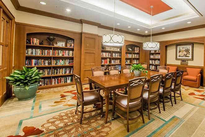 A cozy library with a conference table surrounded by bookshelves and elegant lighting.