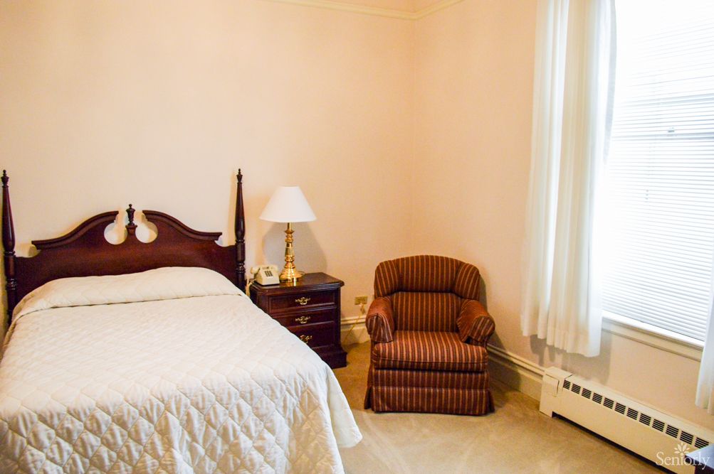 A cozy bedroom with a bed, nightstand, lamp, and an upholstered chair.