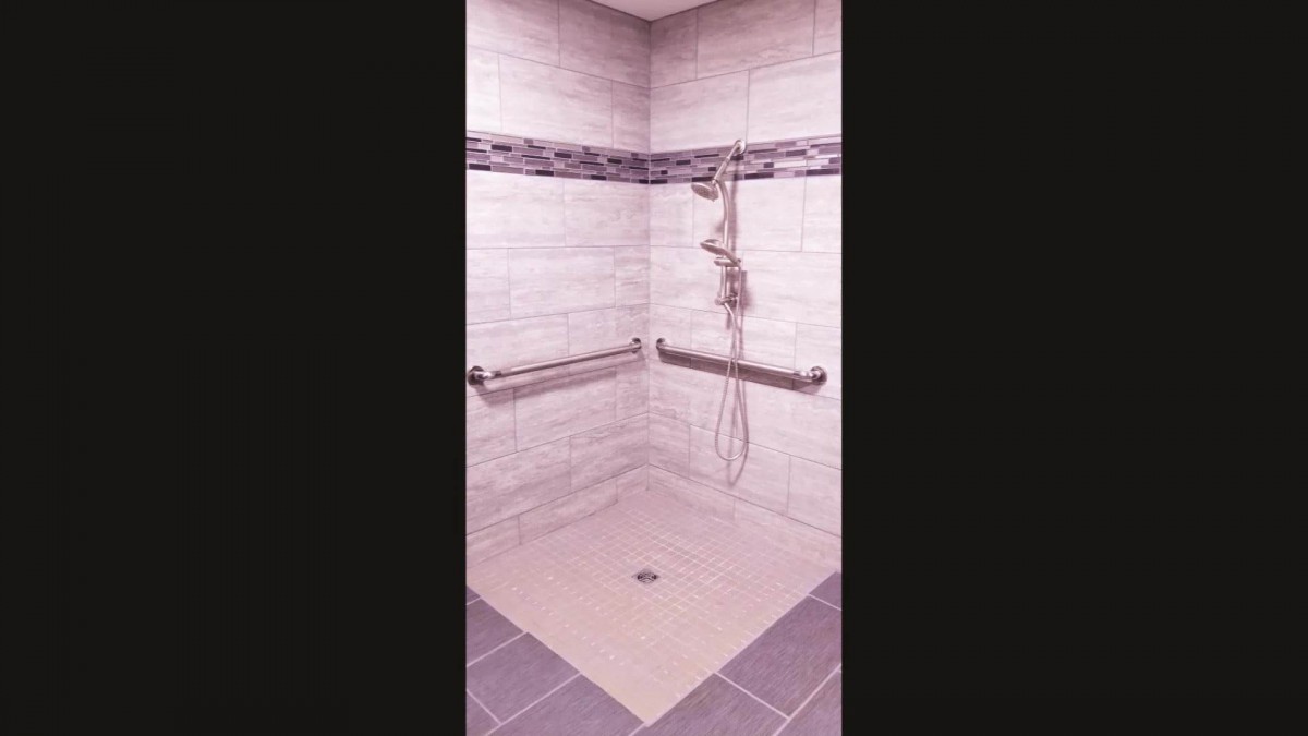A tiled accessible shower with grab bars and a handheld showerhead.