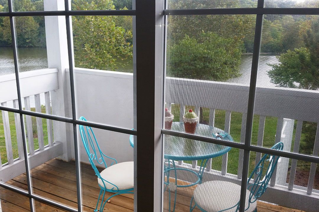 A cozy balcony setup with a small round table and two chairs, overlooking lush green trees.