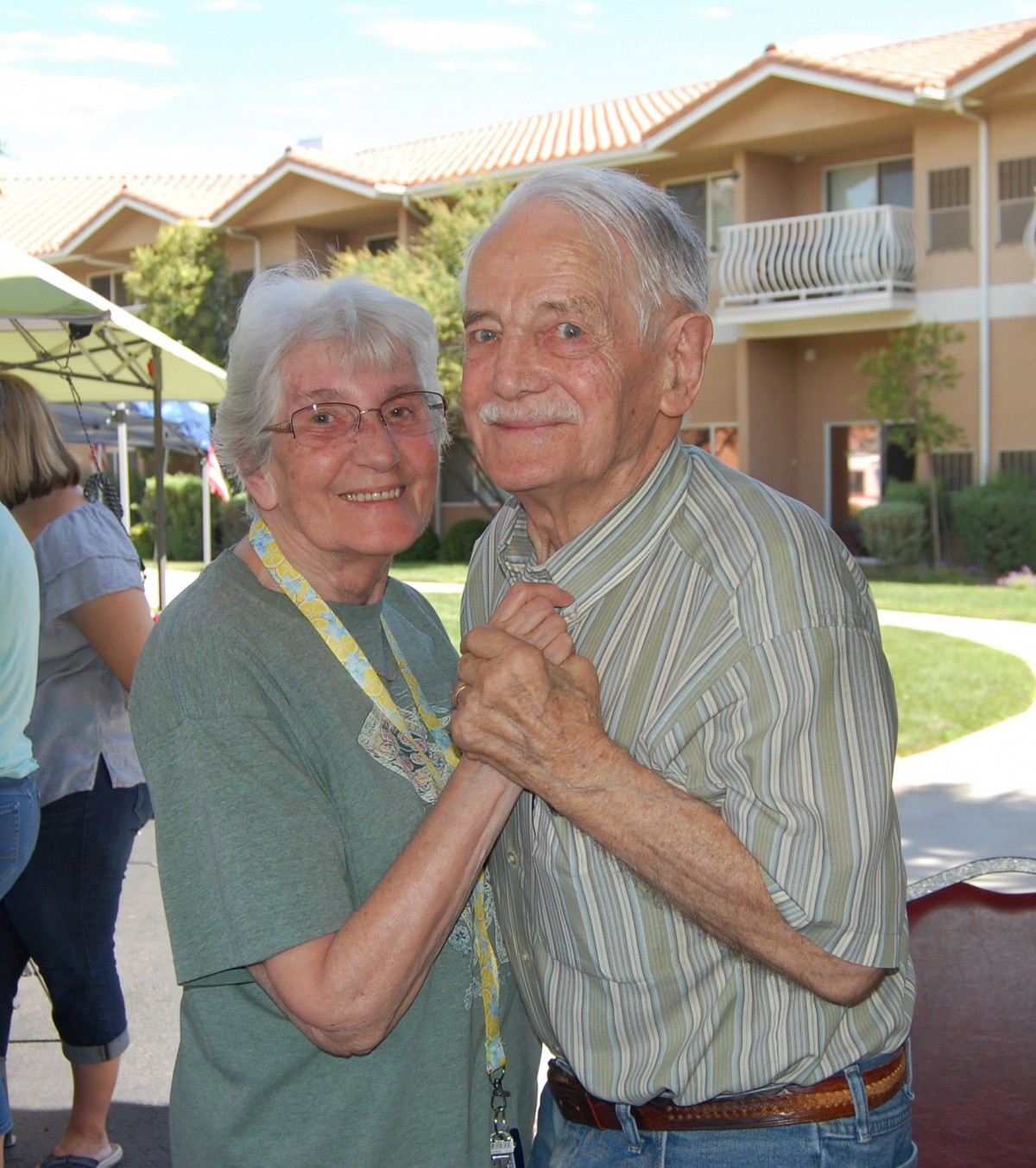 An elderly couple enjoying a dance outdoors on a sunny day.