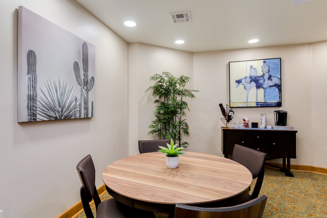 A small meeting room with a round table, four chairs, and decorative plants and artwork.