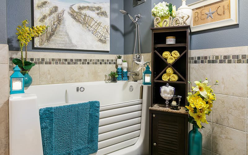 A modern bathroom with a decorative bathtub, vibrant towels, and a stylish shelving unit adorned with flowers and decor.