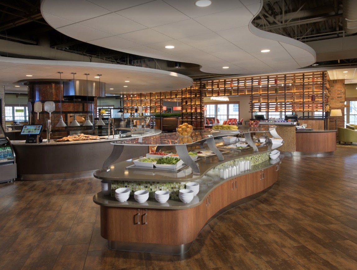 A modern cafeteria with a buffet-style food display and warm lighting.