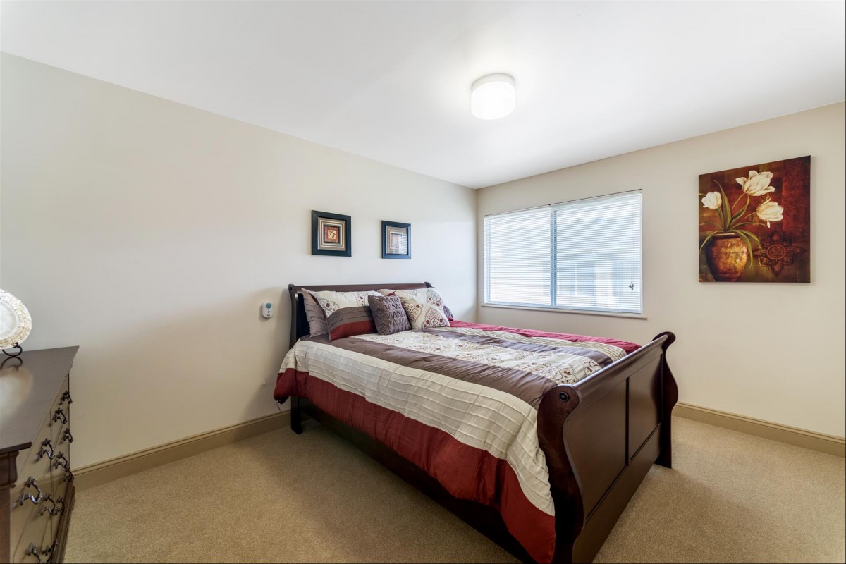 A cozy bedroom featuring a neatly made bed with patterned bedding, adorned with wall art and illuminated by natural light from a large window.