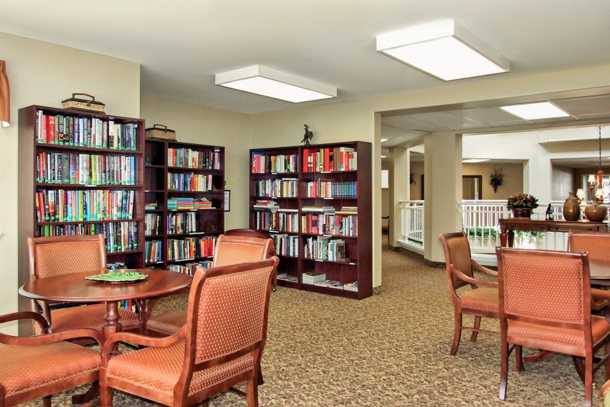 A cozy library reading area with bookshelves, tables, and chairs.
