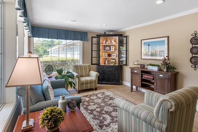 A cozy living room with comfortable seating, decorative shelves, and natural light from a large window.
