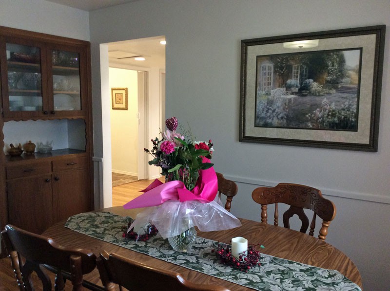 A dining room with a wooden table and chairs, adorned with a bouquet of flowers and a painting on the wall.