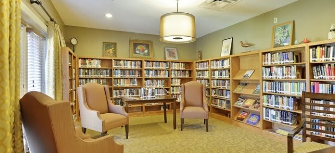 A cozy library reading area with bookshelves, chairs, and a table.