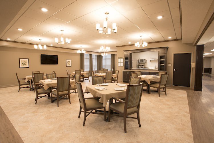 An elegant dining room with neatly arranged tables and chairs, illuminated by chandeliers.