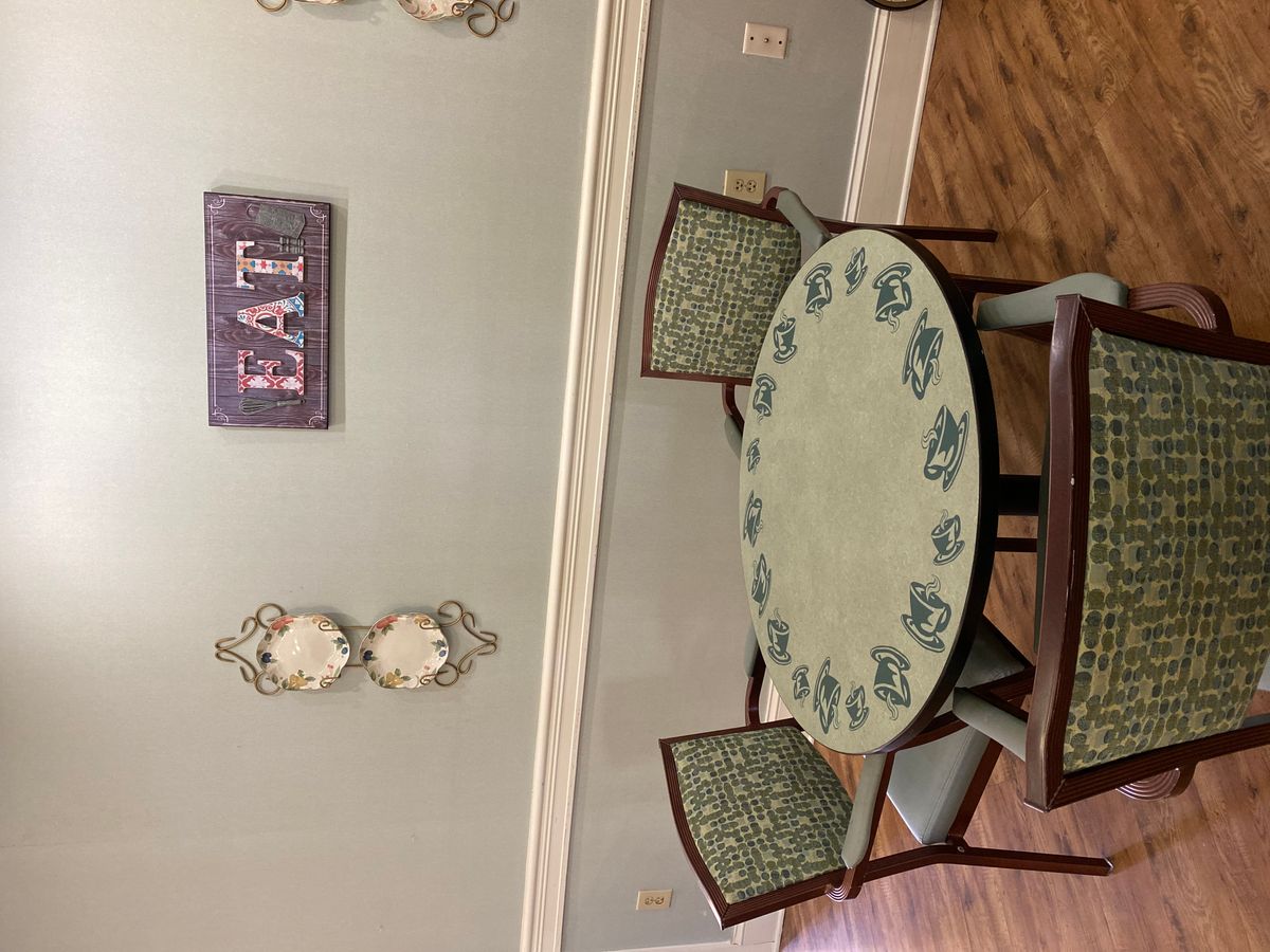 A cozy dining area with an oval table and patterned chairs, complemented by decorative wall accents and a sign that reads 'EAT'.