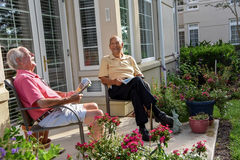 Two people sitting and talking in a garden patio surrounded by plants.