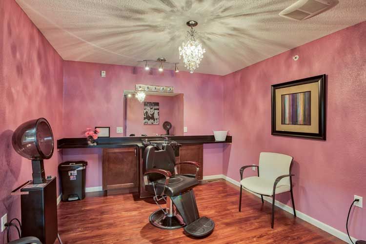 A stylish salon interior with pink walls, a central styling chair, and a chandelier.