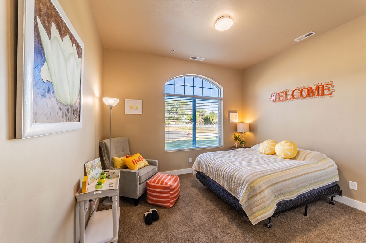 A cozy bedroom with a bed, armchair, and large window letting in natural light.