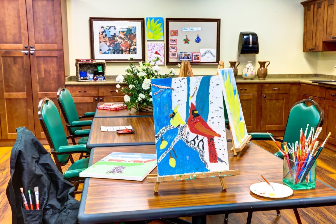 A classroom setting with colorful paintings displayed on easels and tables.