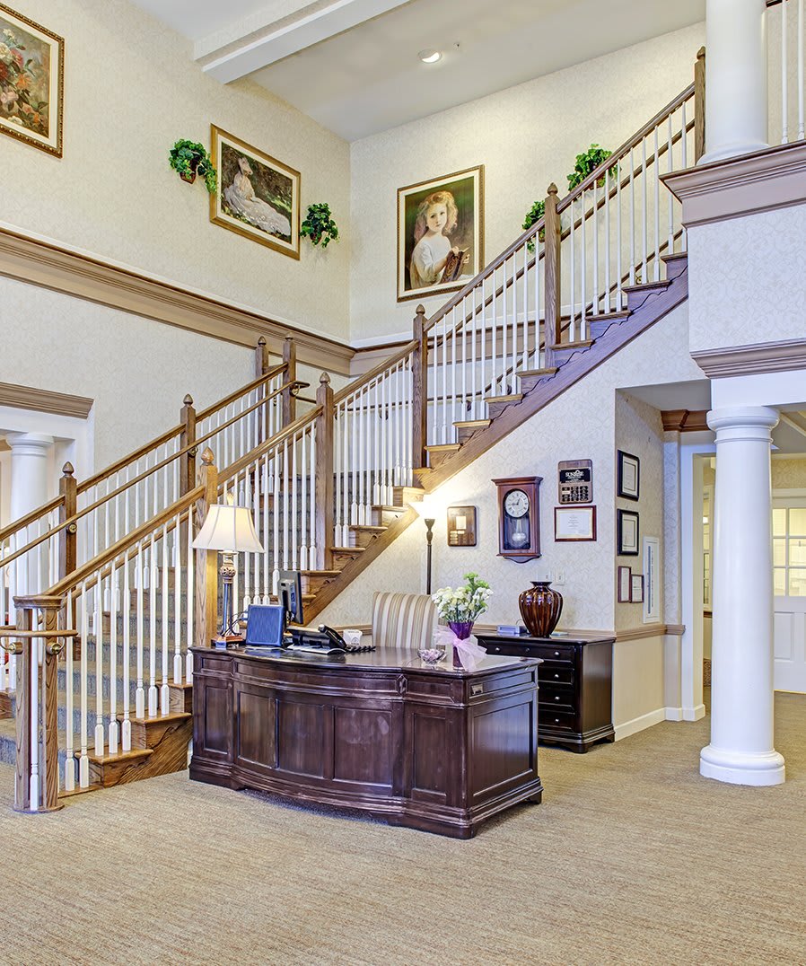 A well-decorated interior office space featuring a wooden staircase, reception desk, columns, and framed art.
