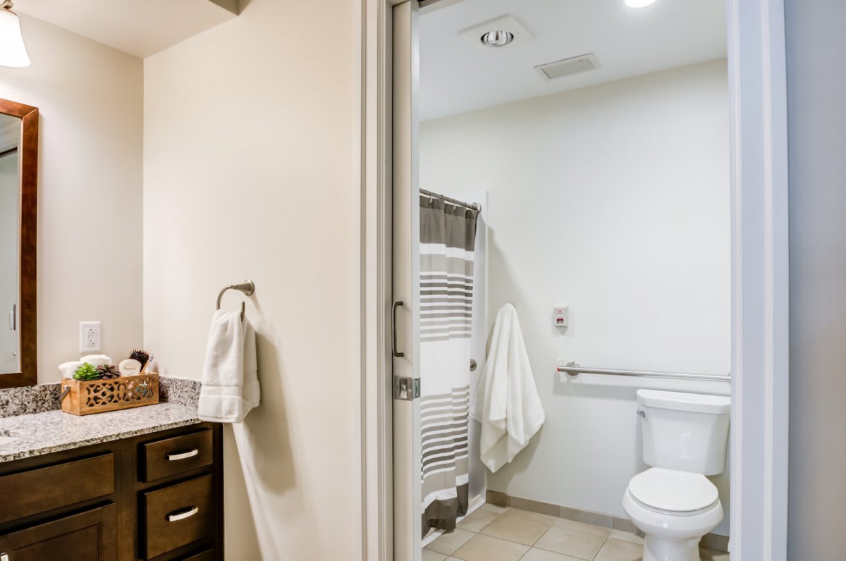 A modern bathroom with accessibility features including a grab bar near the toilet, towels hanging on racks, and a tidy countertop.