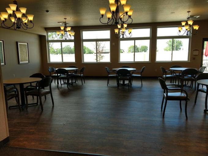 An empty dining room with several tables, chairs, large windows, and chandeliers.