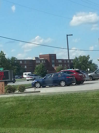 A view of a parking lot with several cars and a building in the background under a clear blue sky.