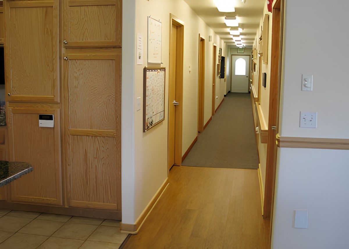 A view down a long, well-lit office hallway with wooden doors and carpet.