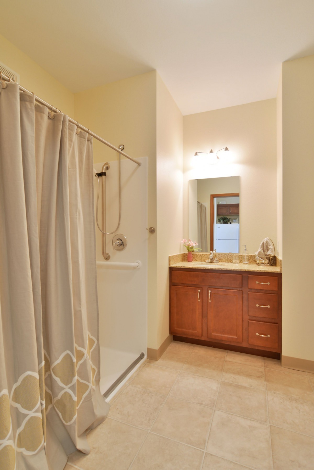 A clean and well-lit bathroom featuring a shower with a curtain, vanity sink area, and a mirror.