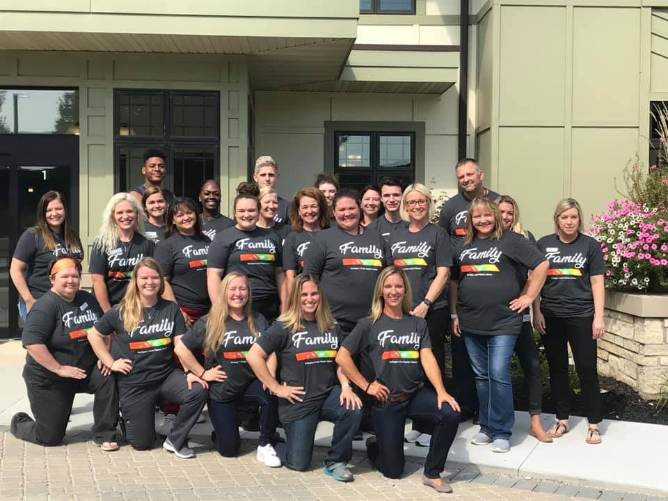 A group of people wearing matching t-shirts posing for a team photo outside a building.