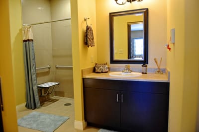 A modern bathroom featuring a sink with a mirror, and a shower area with a towel hanging on the wall.