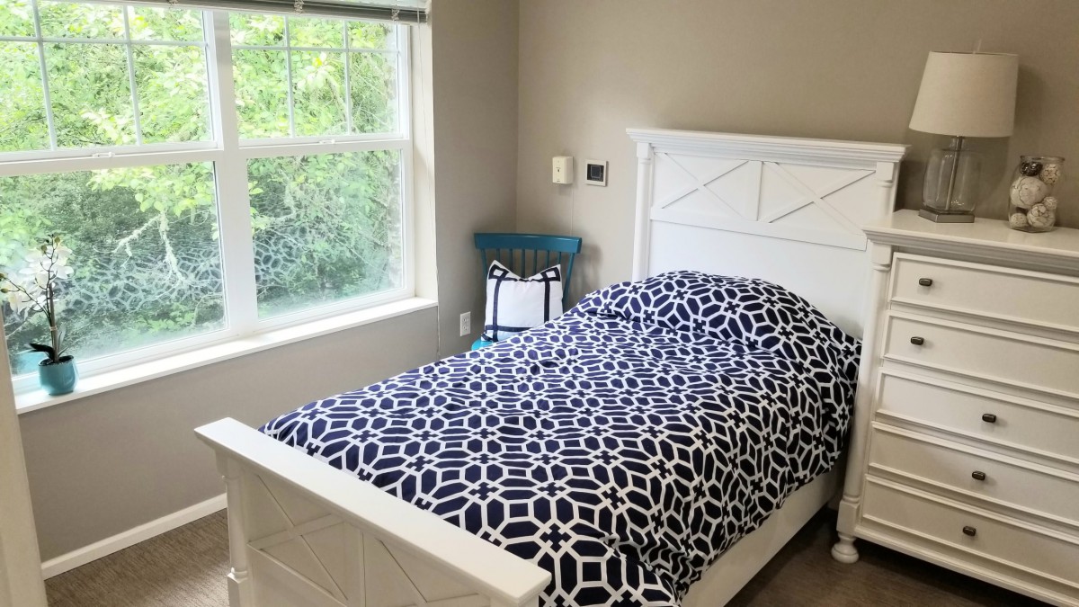 A cozy bedroom with a patterned bedspread and large window allowing in natural light.