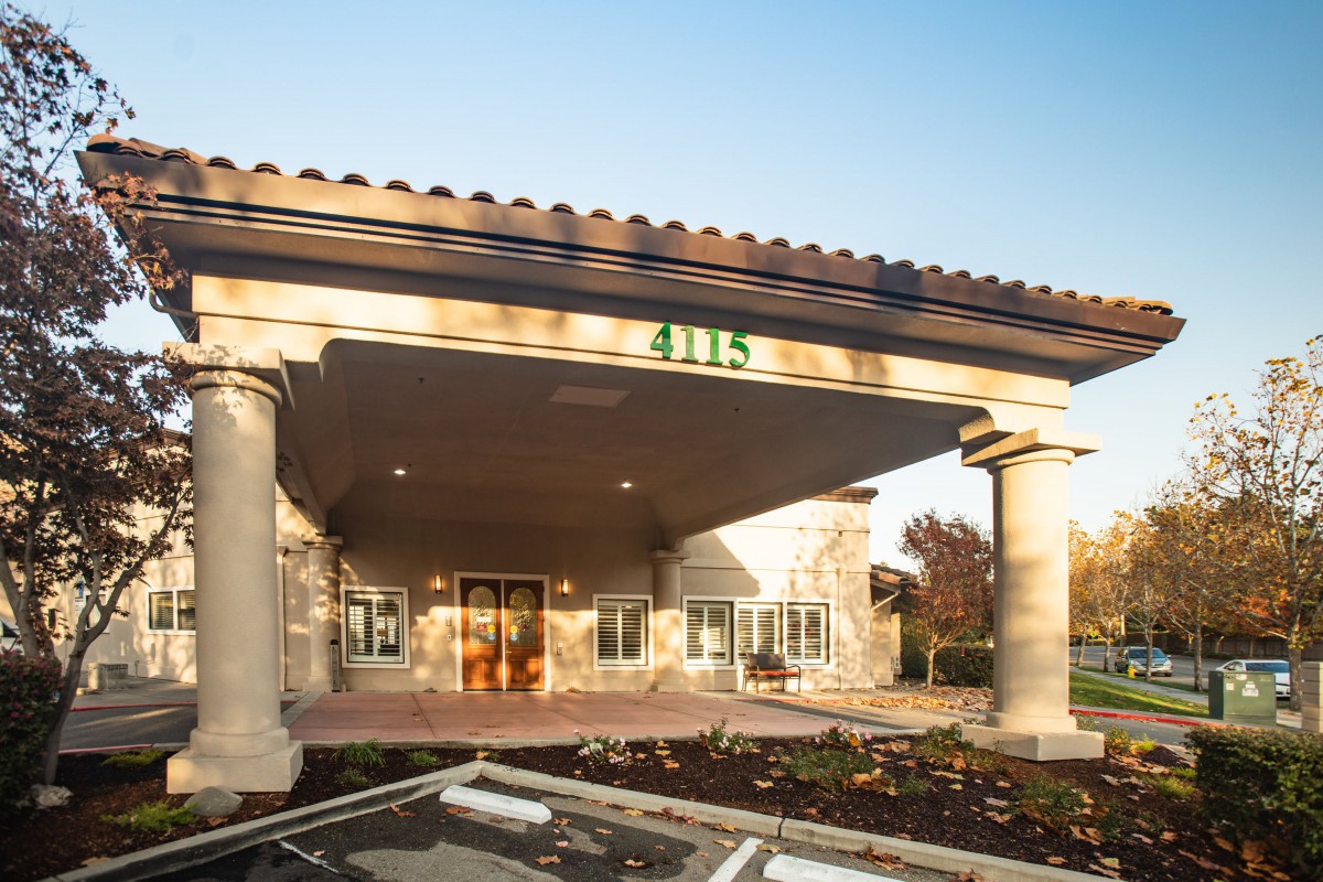 A view of a building entrance with columns and landscaped surroundings.