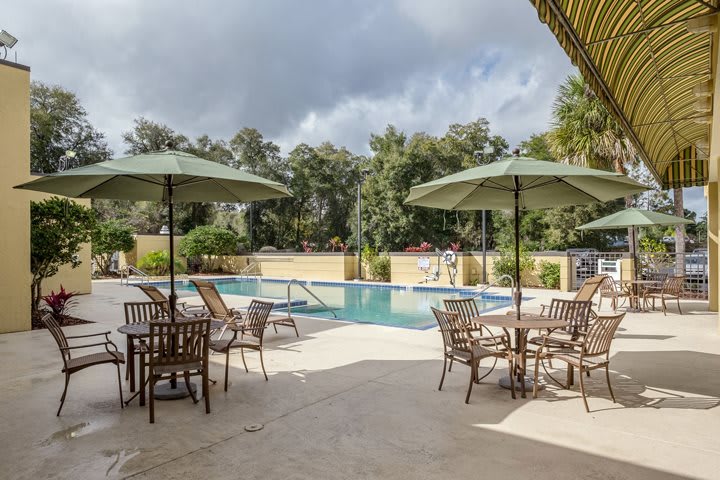 A relaxing outdoor pool area with tables, chairs, and umbrellas set under a cloudy sky.