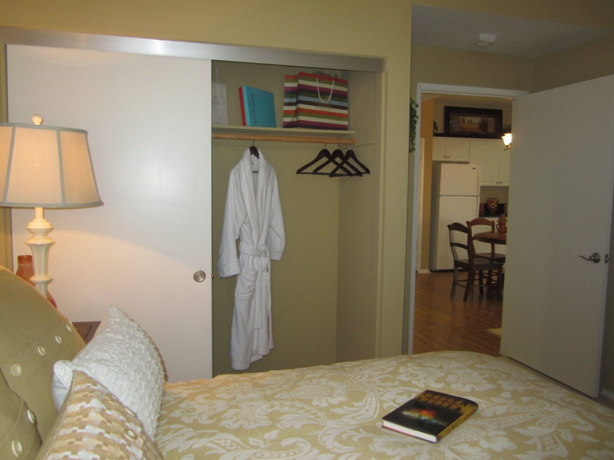 A cozy bedroom with an open closet showing a robe and hangers, adjacent to a kitchen area.