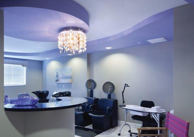 A modern salon interior featuring hair dryer chairs and a manicure station under an elegant chandelier.