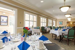 An elegant dining room with tables set with blue napkins and a view of large windows.
