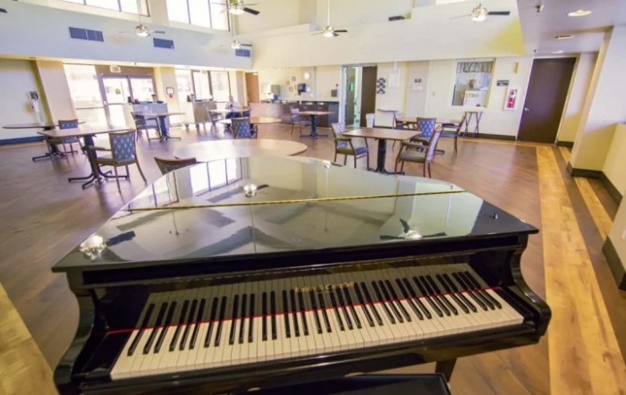 A grand piano in a spacious music room with tables and chairs.