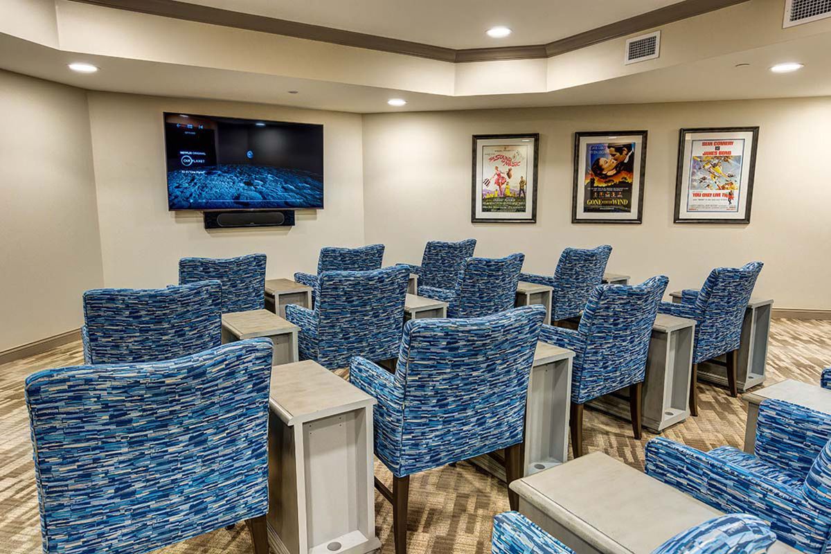 A small theater room with blue patterned chairs and a large TV on the wall.