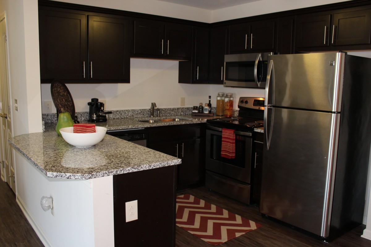 A modern kitchen with dark cabinets and stainless steel appliances.