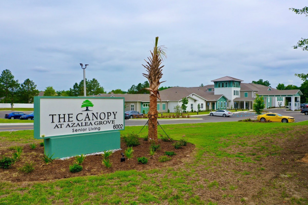 A landscaped area with a sign reading 'The Canopy at Azalea Grove' in front of a modern building.