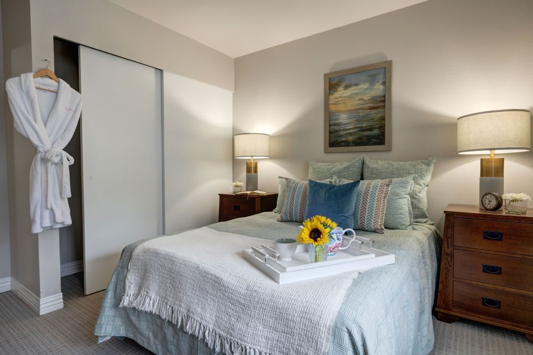 A cozy bedroom with a neatly made bed, soft lighting from bedside lamps, and a sunflower accent.
