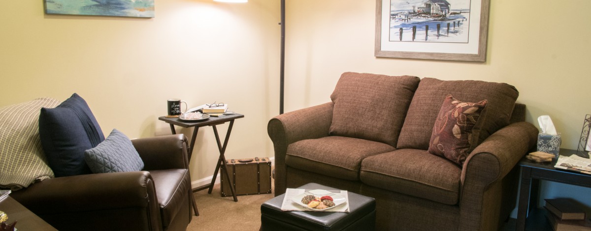 A cozy living room with a brown sofa, a lamp, and a small table adorned with decor.