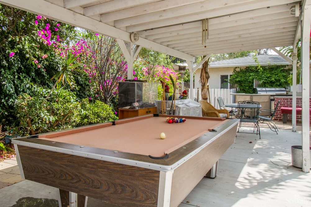 A cozy outdoor patio with a billiards table surrounded by lush greenery and colorful flowers.