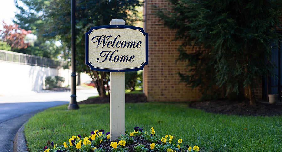 A 'Welcome Home' sign in a garden setting with blooming flowers.