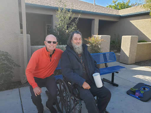 Two men enjoying a sunny day outdoors, one seated in a wheelchair.