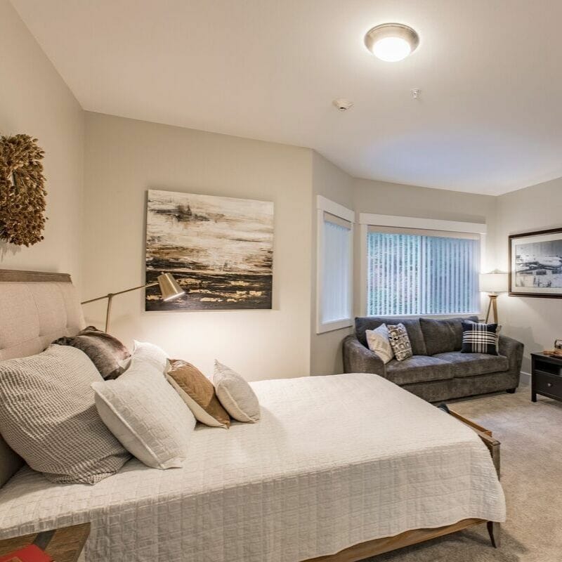 A cozy, modern bedroom with stylish decor featuring a bed, sofa, and artwork on the walls.