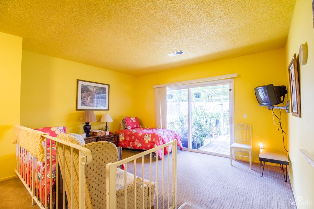 A brightly colored bedroom with yellow walls, featuring a single bed, chair, and sliding glass door.